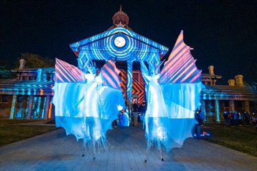 Snow angel stilt walkers in front of the illuminated Bathurst Courthouse.