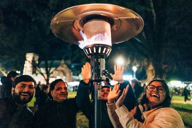 Group of friends warming up around a heater in the park.