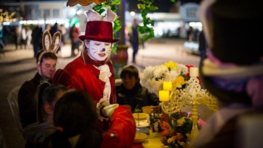 Children sitting around a table for a Mad Hatters Tea Party with a performers dressed as Alice in Wonderland characters.