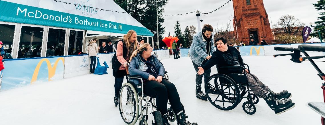 Two festival goers in wheelchairs being pushed by their carers on the McDonald's Bathurst Ice Rink.