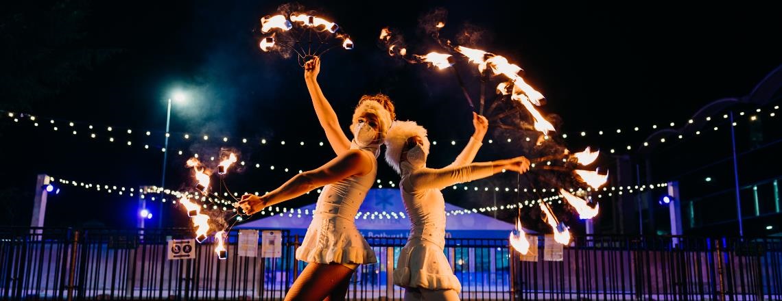 Two fire dancers dressed in warm white winter clothing posing with their fire batons.