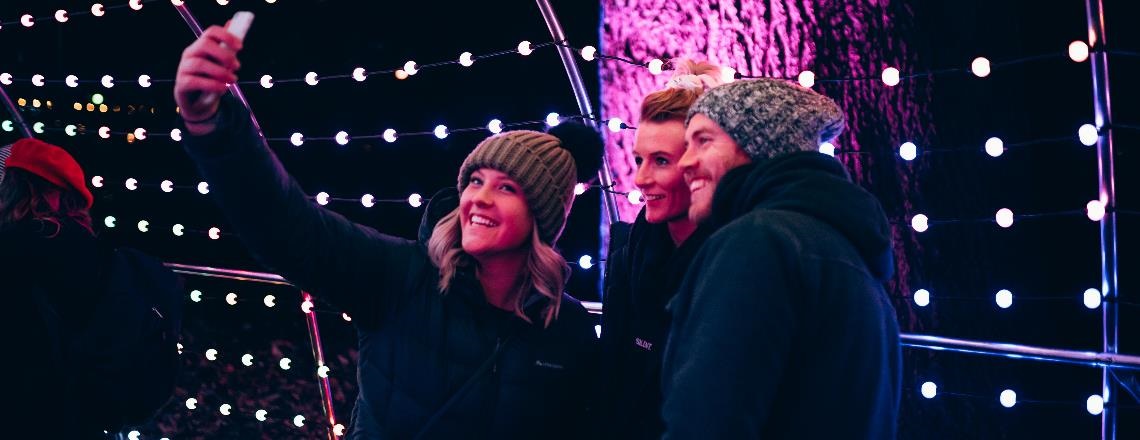 Three people posing for a selfie inside a light tunnel installation.