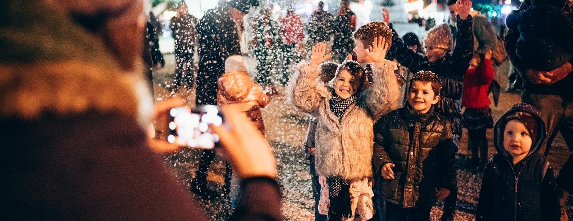 Kids playing under the snow falling and having their picture taken.