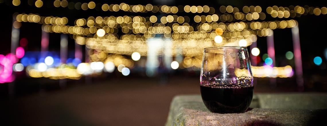 Reusable Bathurst Winter Festival wine glass sitting on a sandstone block with festoon lighting in the background.