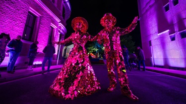 Two dress up characters dressed in reflective mirror outfits wandering through the lights at the festival.