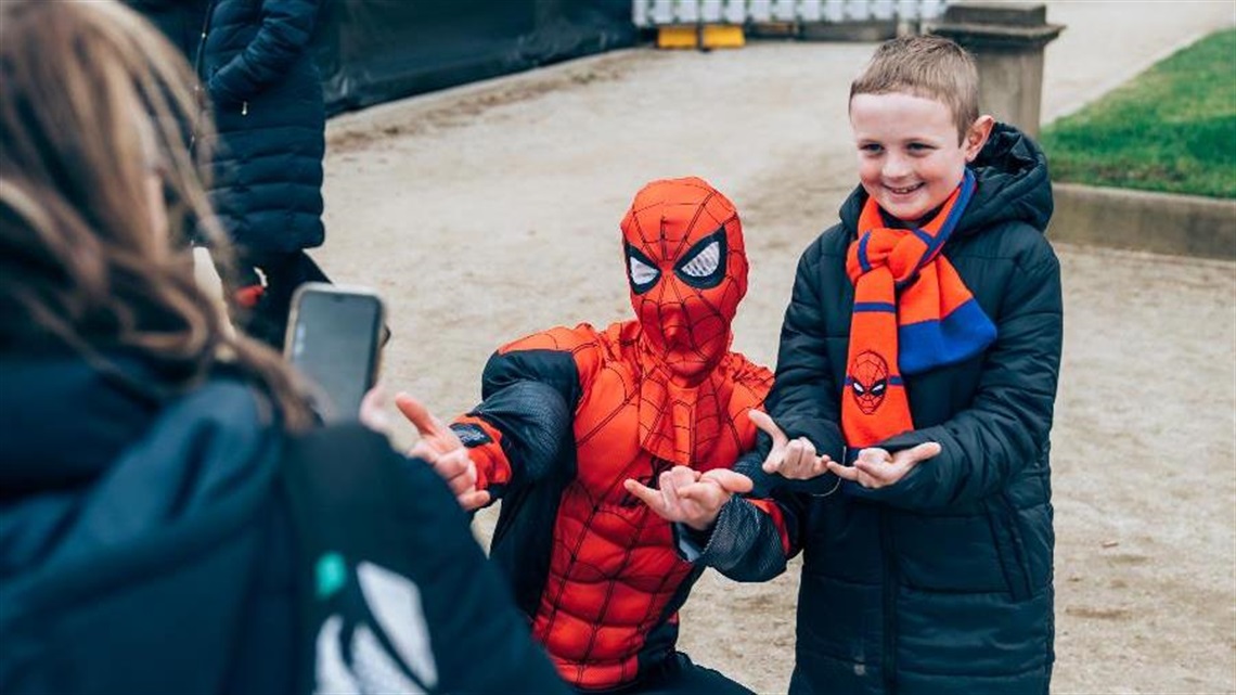Mother taking an photo of her son posing with Spiderman dress up character on Kids Day.